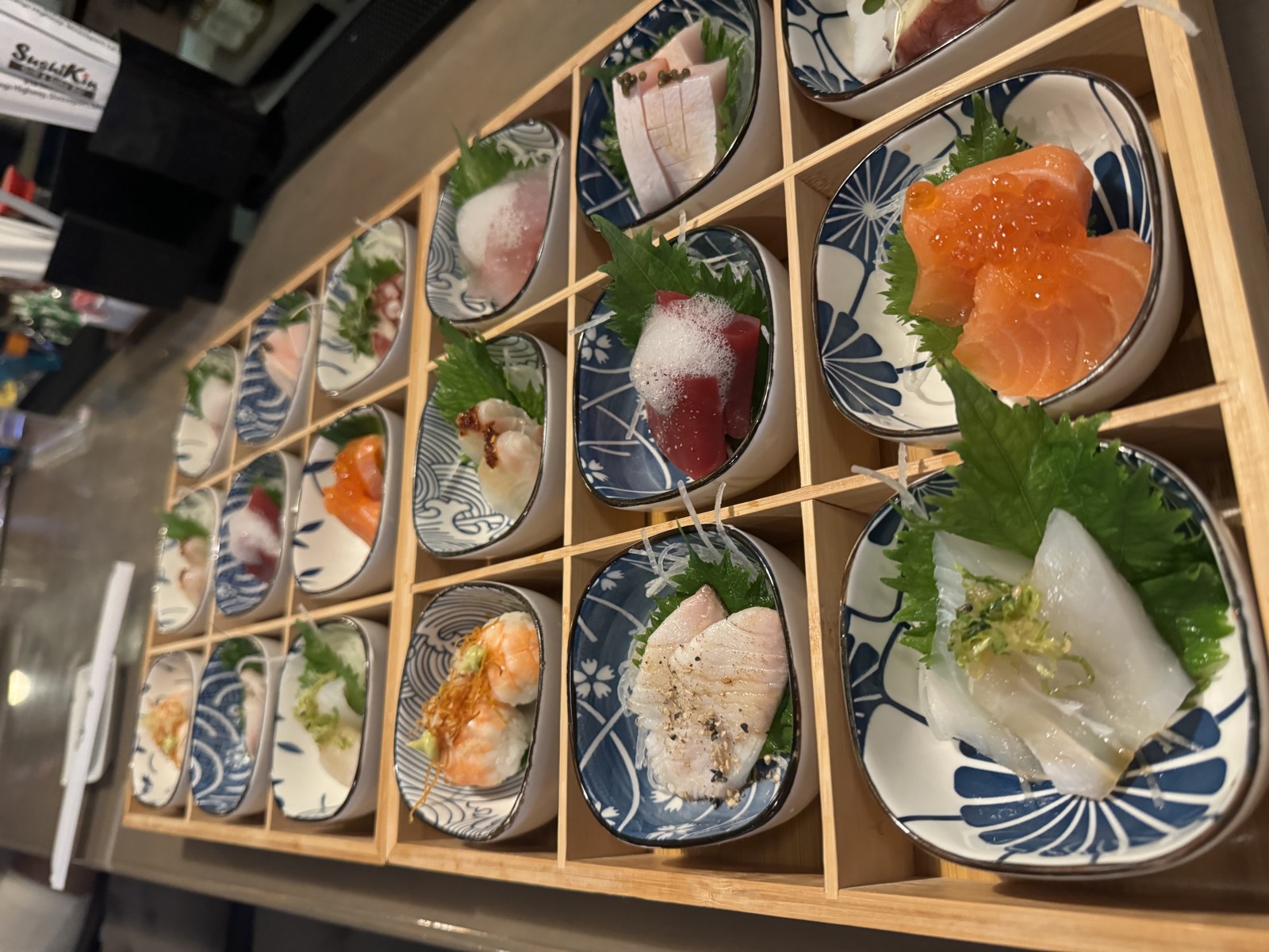 The Kinakase bento collection — a wooden box of eighteen small sashimi and nigiri dishes in patterned bowls